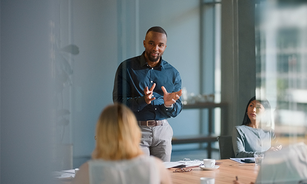 A male individual speaking to a group in a board meeting