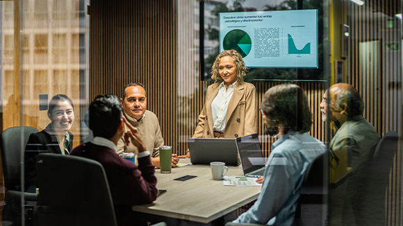 An image of a board meeting with people in a room with a digital screen behind them